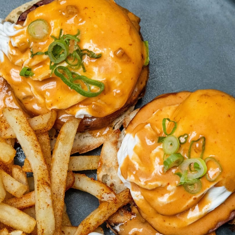 Two burgers topped with melted cheese, sour cream, and green onions, served with seasoned fries.